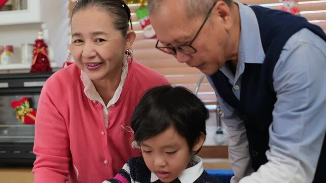 Happy Asian family spending times to prepare Chritsmas and Happy news year Celebrete. kids parent and grandparent doing ginger breads and bakery enjoy and dancing in kichen at home