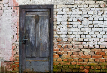 Rustic brick wall featuring a weathered blue wooden door with whitewash remnants
