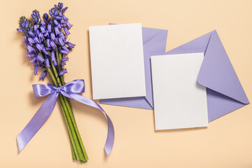 A bouquet of lavender spring scilla, two lilac envelopes and blank cards on a beige background....