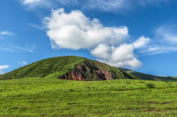 Green meadow against the backdrop of a green hill. Blue sky with clouds. Journey into the wild.