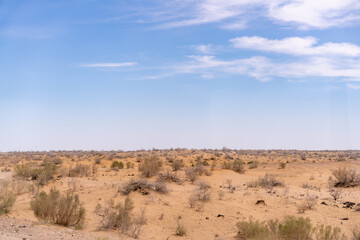 A desert landscape with a clear blue sky. The sky is dotted with clouds, and the sun is shining brightly. The scene is peaceful and serene, with the vast expanse of sand