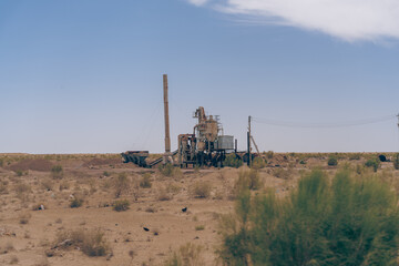 A large industrial plant sits in a desert landscape. The plant is surrounded by a fence and a power line. The scene is desolate and barren, with no signs of life