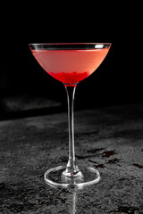 A vibrant red cocktail in a classic martini glass against a dark, moody background.