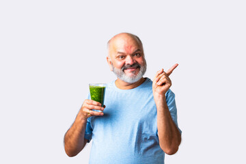 Elderly senior old Indian asian man eats green juice or drinking vegetable juice in a glass