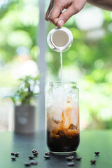 pouring milk into a glass of coffee