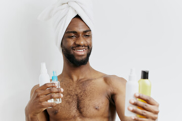 Man with towel on head presenting hair care products in bathroom