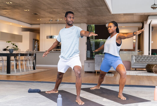 Practicing yoga together, young couple standing in warrior pose on mats at home