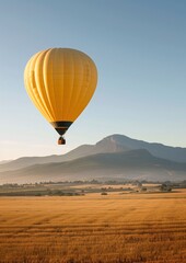 Obraz premium Orange Hot Air Balloon Flying Over Scenic Field with Mountains at Sunrise