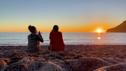 couple sitting on the beach with glass of wine enjoying sunset