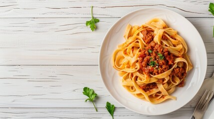 A plate of fettuccine pasta with bolognese sauce sits on a white wooden table, viewed from directly above