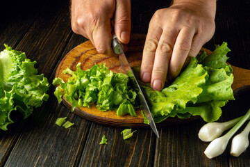 Chef cutting lettuce leaves on wooden board with knife in hand before preparing tasty breakfast. Vegetable diet concept