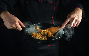 Chef frying fish in a frying pan for breakfast. Concept on black background of cooking fish dish.