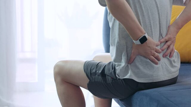 Young man is experiencing back pain while sitting on a couch