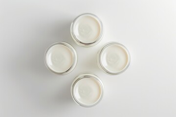 Four jars of cream sit on a white surface, awaiting use or display