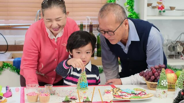 Happy Asian family spending times to prepare Chritsmas and Happy news year Celebrete. kids parent and grandparent doing ginger breads and bakery enjoy and dancing in kichen at home