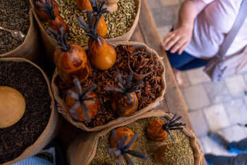 A woman is walking past a table with a variety of spices and herbs. The spices are in small bags and containers, and there are several different types of spices on the table