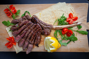 Juicy and tasty tomahawk arranged on traditional carasau Sardinian bread with lemon and tomatoes