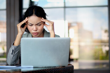 Tensed businesswoman puts head in hands in front laptop at office workplace. Woman suffers from a...