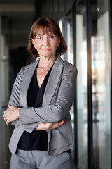 Happy smiling senior businesswoman in suit standing with arms crossed in front of office. Elderly successful female boss working at workplace. Portrait of Caucasian white mature woman worker.