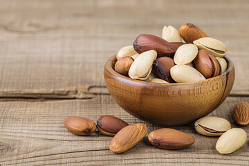 A wooden bowl filled with pine nuts and pistachios on a rustic wooden table.