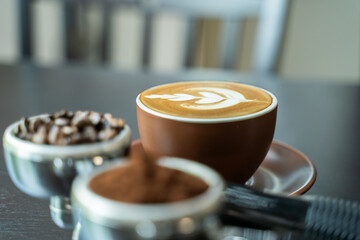 Side view of a cup of cafe latte with baskets of coffee beans and grind coffee