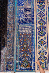 A blue and white tile wall with Arabic writing. A person is pointing at the wall