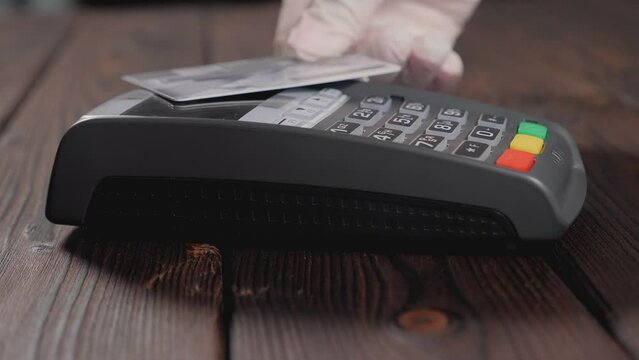 Close-up of a woman in medical gloves paying with a card for medicines in a pharmacy on a wooden background.