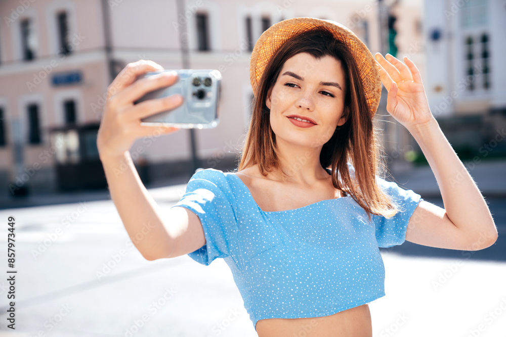 Poster Young beautiful smiling hipster woman in trendy summer blue clothes. Sexy carefree woman posing on the street background at sunset. Positive model outdoors. Cheerful and happy and hat, take selfie