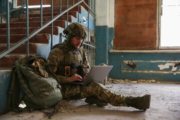 Military mission. Soldier in uniform using laptop inside abandoned building