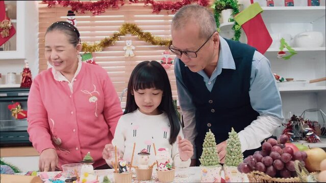 Happy Asian family spending times to prepare Chritsmas and Happy news year Celebrete. kids parent and grandparent doing ginger breads and bakery enjoy and dancing in kichen at home
