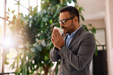 Ill entrepreneur using  tissue while sneezing in  hallway.