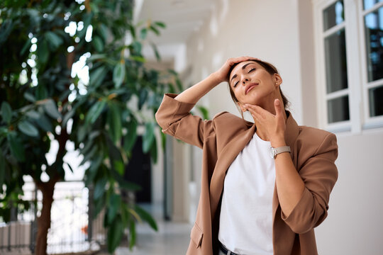 Young businesswoman stretching her neck in office hallway.