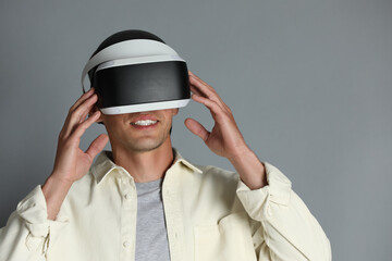 Smiling man using virtual reality headset on gray background, space for text