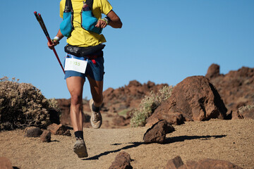 Trail running runner man on endurance run with hydratation trail vest on volcano mountain. Ultra marathon race athlete on volcanic rocks path in mountains landscape