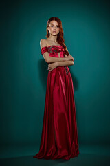 A young girl with exquisite makeup and good skin, a stylish hairstyle posing in the studio in a red dress on a green background