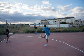 Teenagers playing soccer on outdoor court, one kicking ball