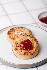 Hot Toasted Crumpets with piece of butter on a plate with strawberry jam. Perfect tasty breakfast popular in England, UK