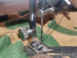 Old sewing machine needle drive on camouflage fabric cloth closeup