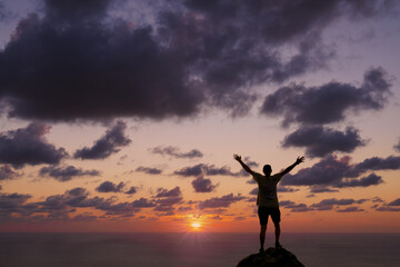 Fototapeta premium Man at sunset. Man with arms up at sunset in front of the sea.