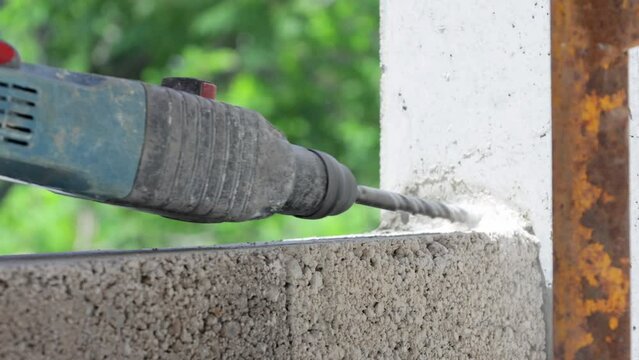 Close-up view of hands holding a perforator and drilling into a wall at a construction site.