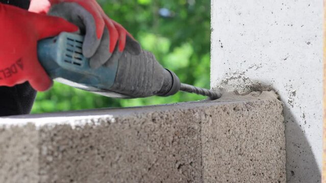 Close-up view of hands in gloves operating a perforator to drill into a wall at a construction site.