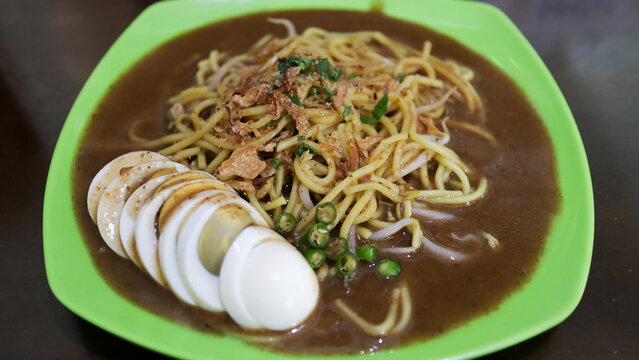 raditional Mie Lendir Noodle Dish from Riau Islands Batam Indonesia served on a green plate with boiled egg slices and garnished with fried shallots and green chilies