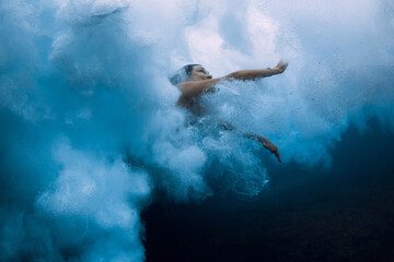 Surfer girl dive underwater in ocean washing under dangerous wave foam