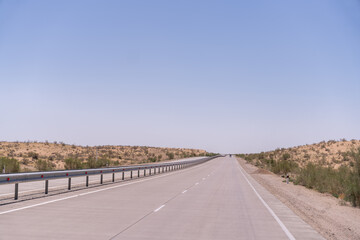 A long, empty road with a blue sky above. The road is lined with a fence and there are no cars on it
