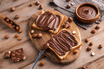 Board of bread with chocolate paste and hazelnuts on wooden background