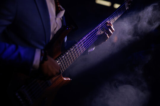 A musician strumming an electric bass guitar on a dimly lit concert stage