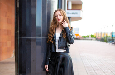 Obraz premium A young smiling girl in a good mood walks around the city. Teenage girl, portrait against the background of houses and roads. Fashionable youth style trend.