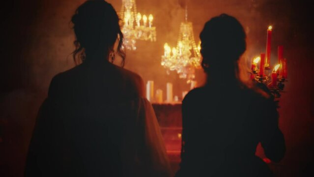 two women vintage clothes white red dress. Fantasy beauty Sexy girl walking in night dark room hand holding old style candlestick candles burning light back rear view. Gothic Mystery woman queen. 4k.