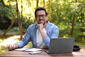 Smiling freelancer with laptop at table outdoors. Remote job
