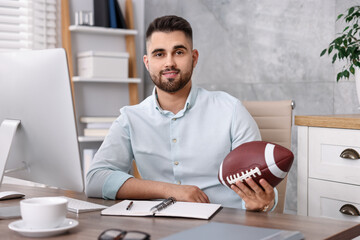 Young man with american football ball at table in office
